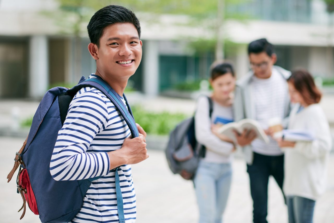 Estudiante sonriente con mochila en el campus junto a sus compañeros